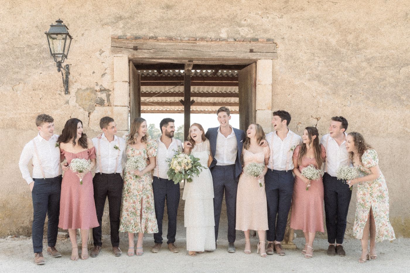 A wedding group photo in front of a rustic French barn