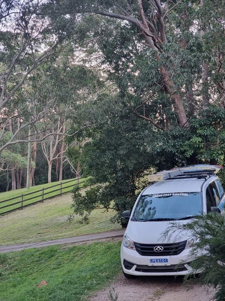 A White Van Is Parked In A Grassy Area Next To A Tree — Local Pest Control Illawarra in Dapto, NSW