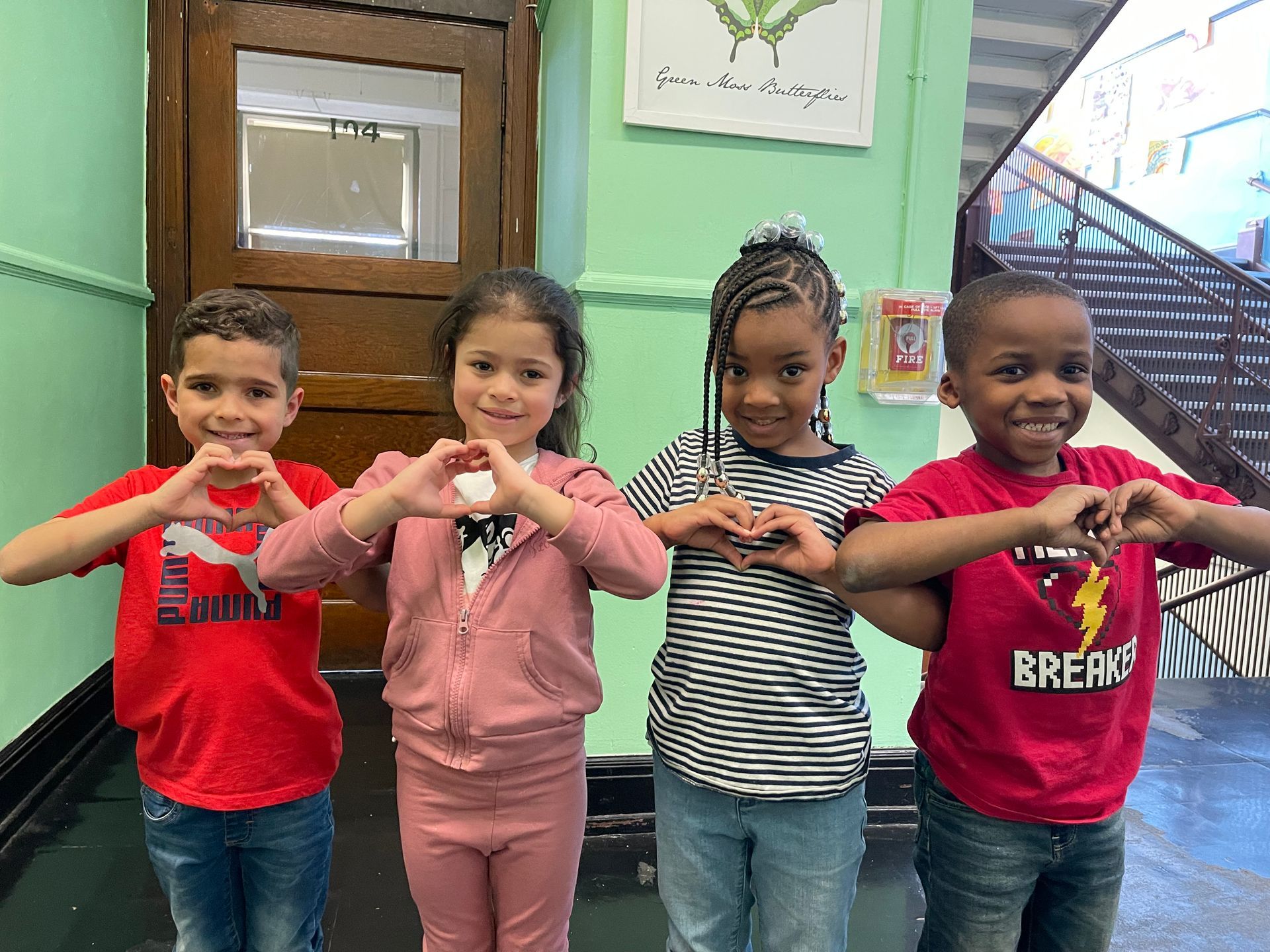 A group of Montessori children are making a heart shape with their hands.