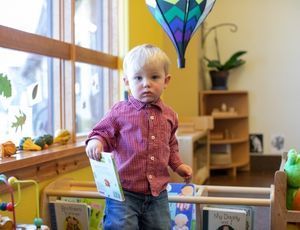 Montessori child reading a book in cozy space, building focus, imagination, and love of stories.

