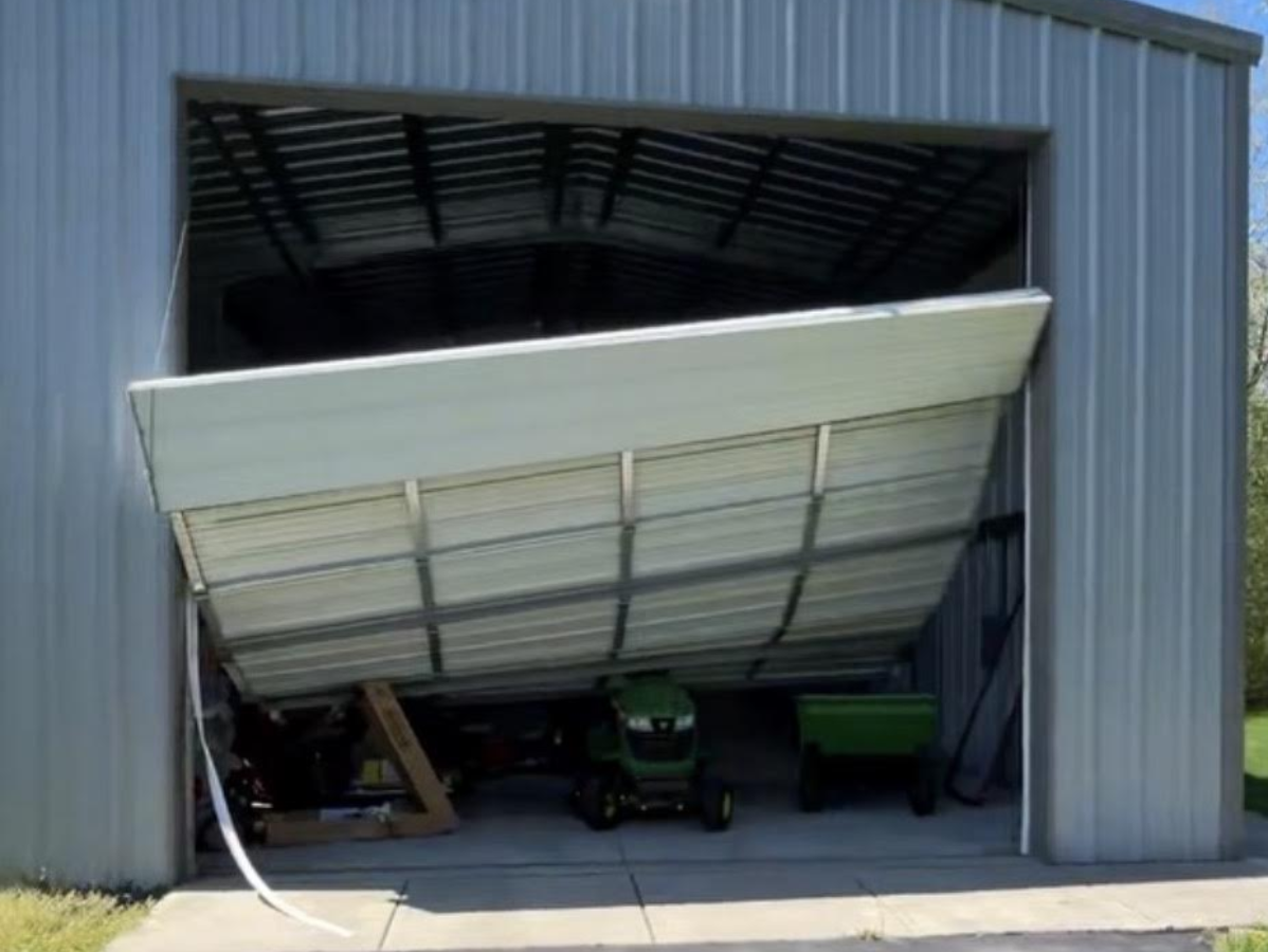Partially collapsed metal garage door blocking a shed opening, with equipment visible inside