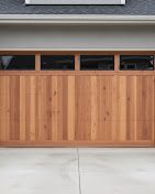 Wooden garage door with narrow windows beneath a gray roofline and concrete driveway