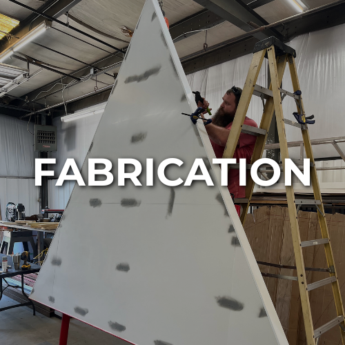 Man using a tool on a large, triangular white structure inside a workshop | metal sign maker near me