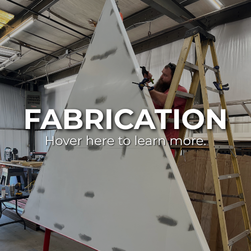 Man on a ladder working on a large white triangular structure in a workshop | custom sign fabrication