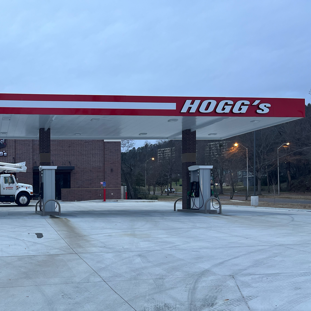 Hogg's gas station with red and white canopy, gray pumps, overcast sky, and work truck | local sign company near me