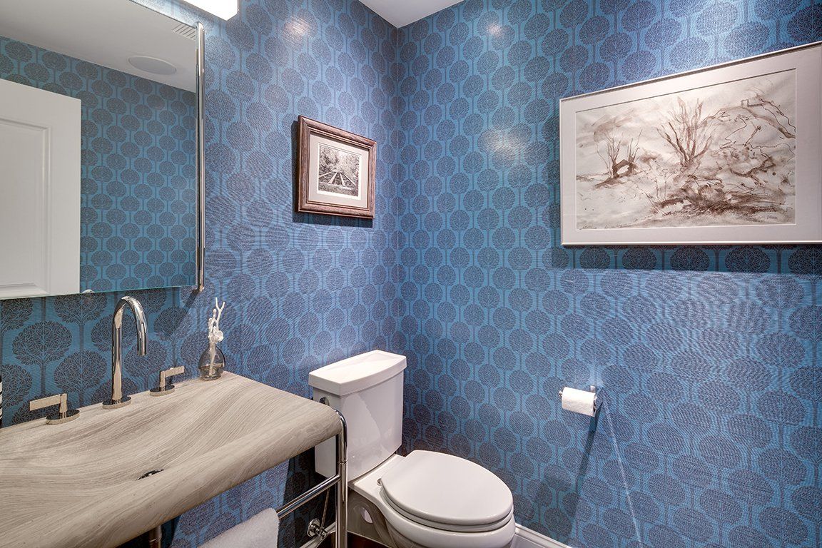 A bathroom with blue walls , a toilet , sink and mirror.