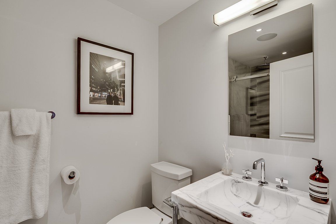 A bathroom with a toilet , sink , mirror and picture on the wall.