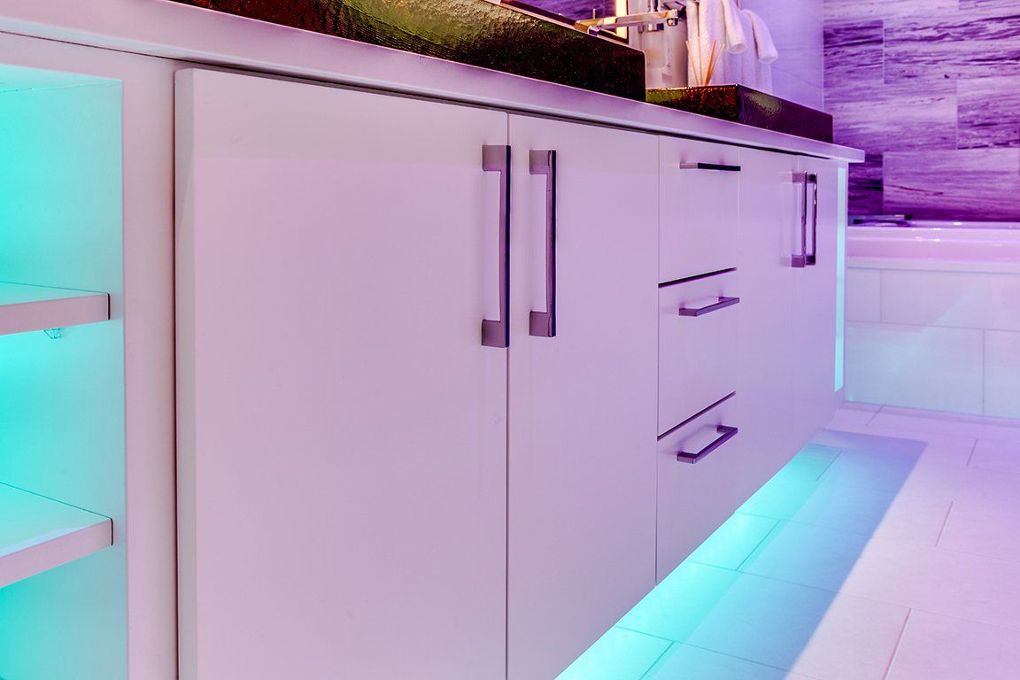 A kitchen with white cabinets and purple and blue lights.