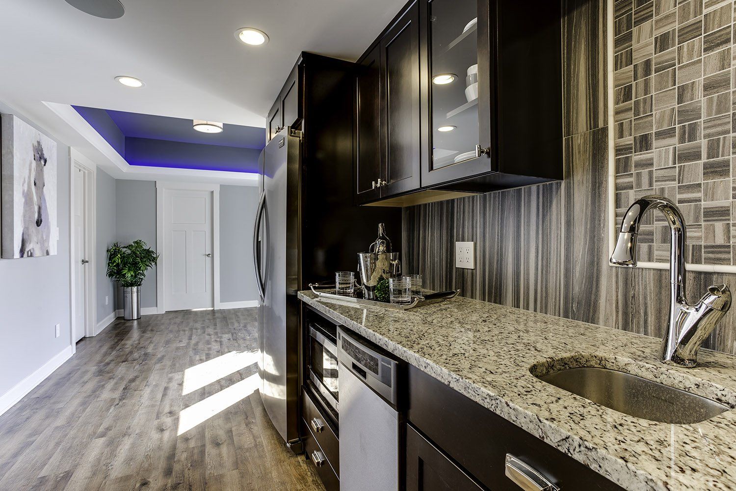A kitchen with granite counter tops , stainless steel appliances , and black cabinets.