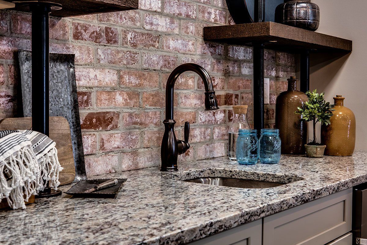A kitchen with granite counter tops , a sink , and a brick wall.