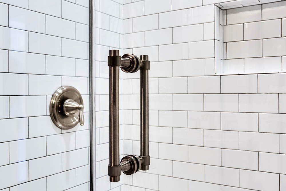 A shower with white tiles and a black handle on the door.