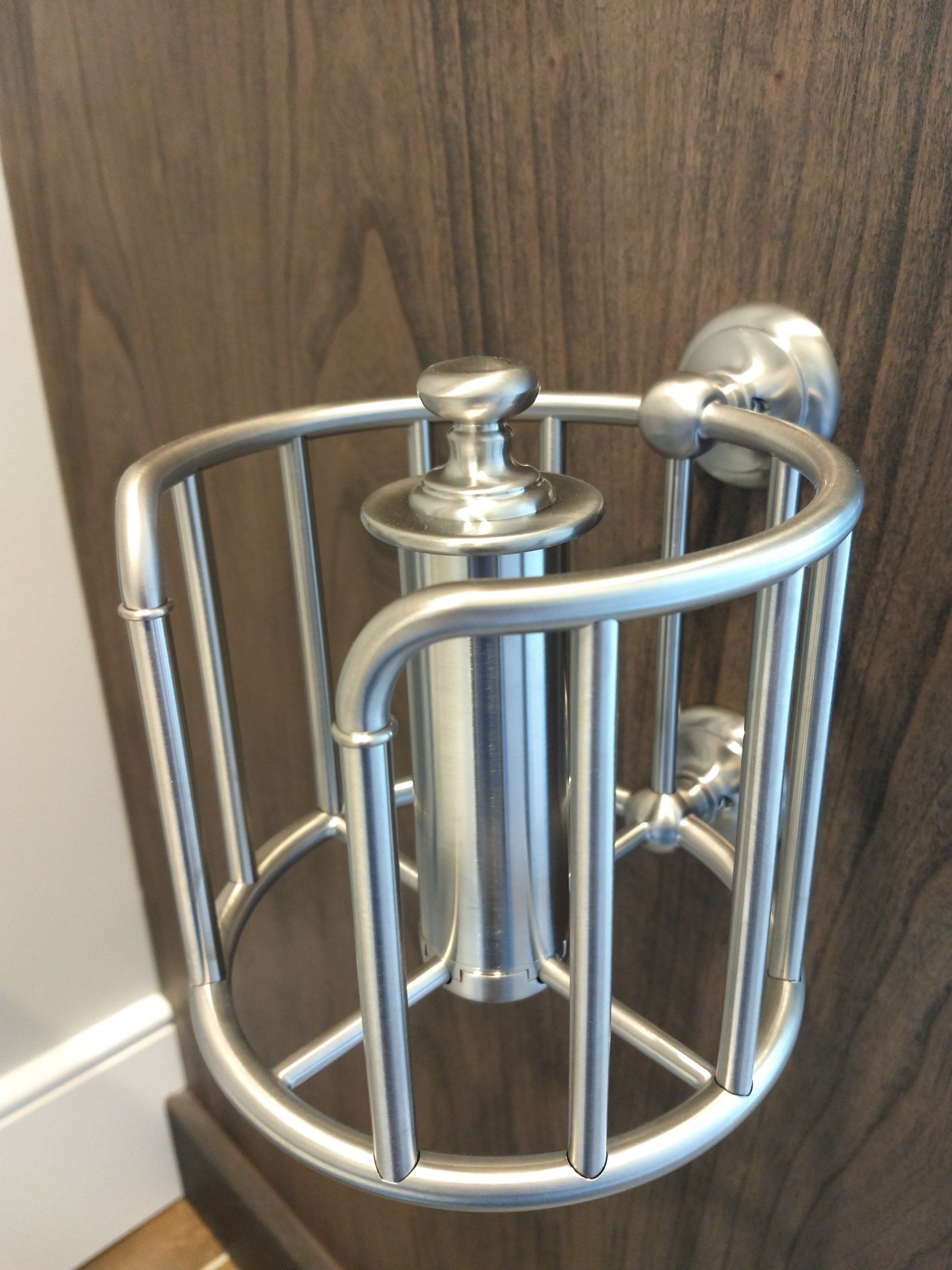 A stainless steel toilet paper holder is attached to a wooden wall