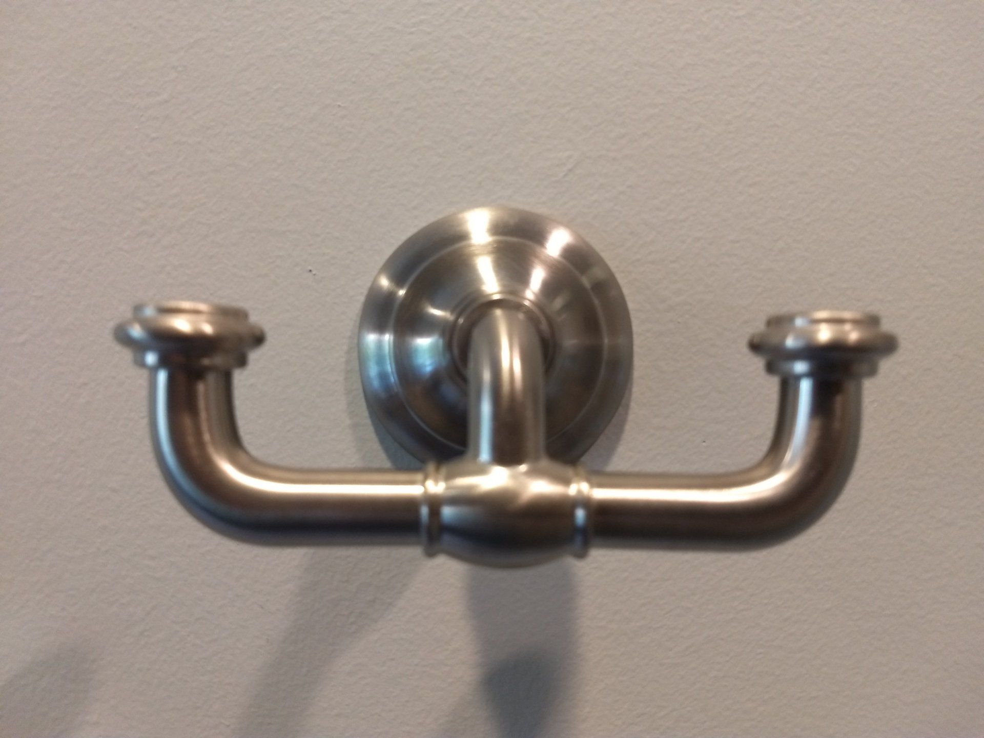 A stainless steel hook is hanging on a white wall