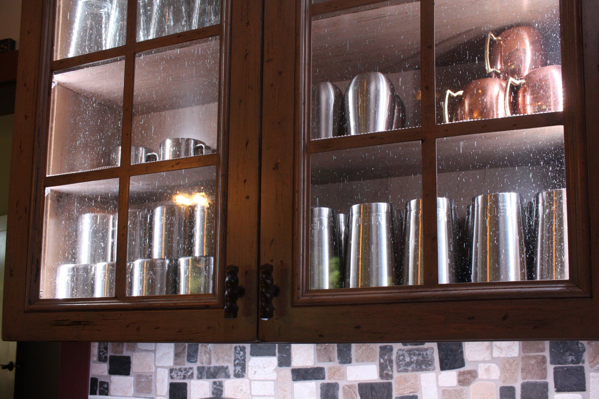 A kitchen cabinet with a glass door filled with copper pots and pans
