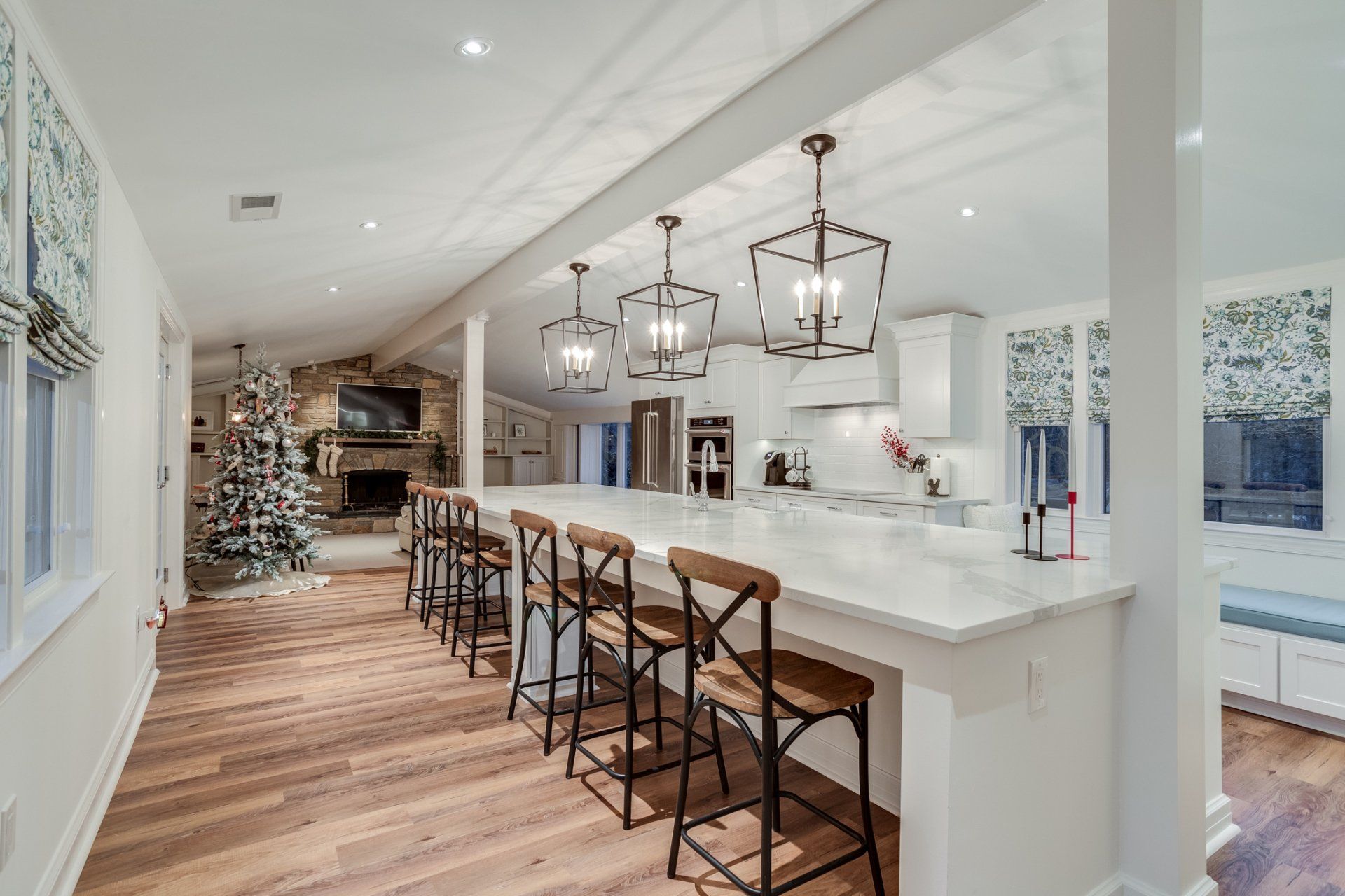 A kitchen with a long island and stools and a christmas tree in the background.