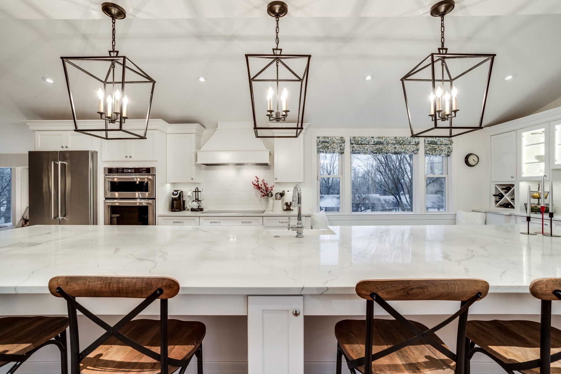 A kitchen with white cabinets , stainless steel appliances , a large island , and three chairs.