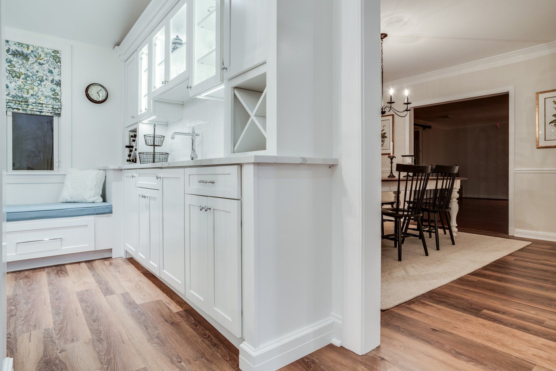 A kitchen with white cabinets and hardwood floors leading to a dining room.
