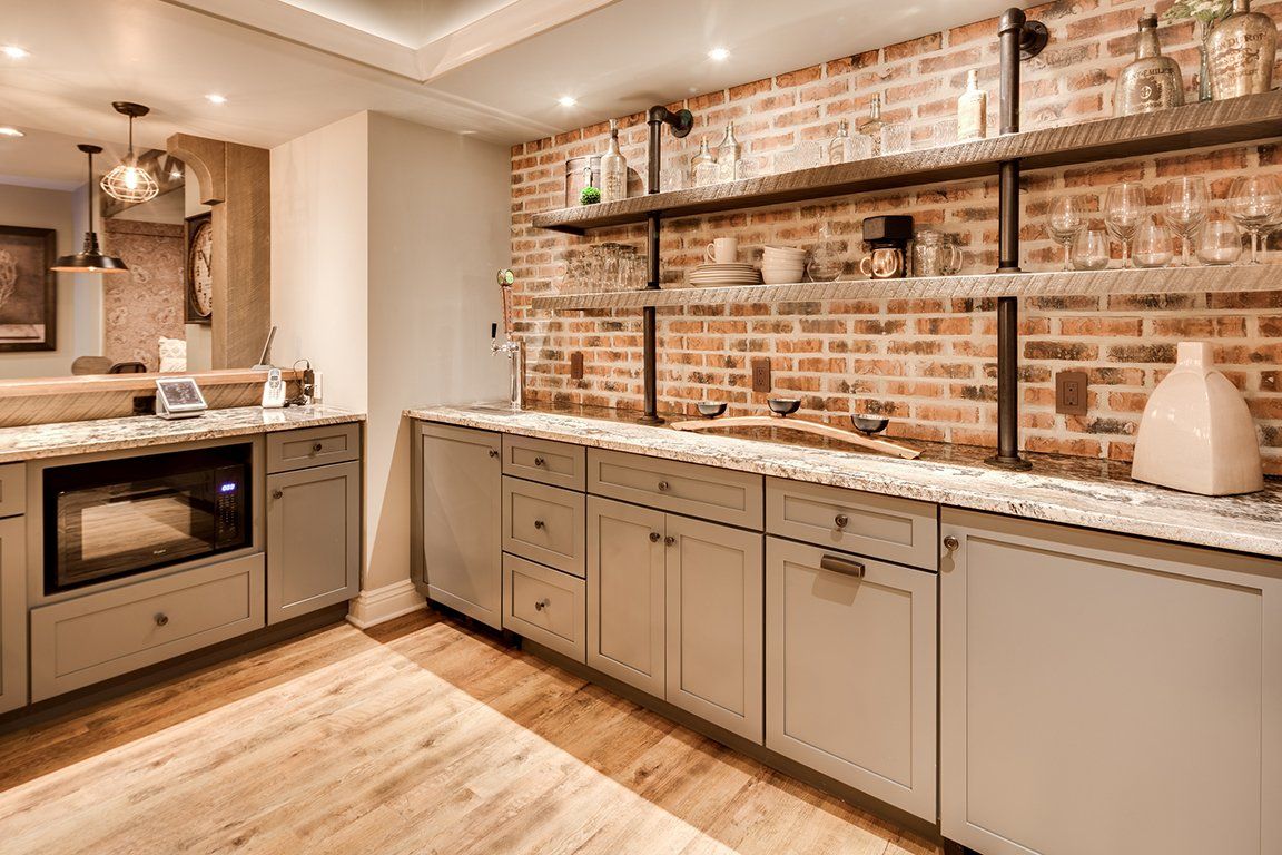 A kitchen with a brick wall , white cabinets , a sink , and a microwave.