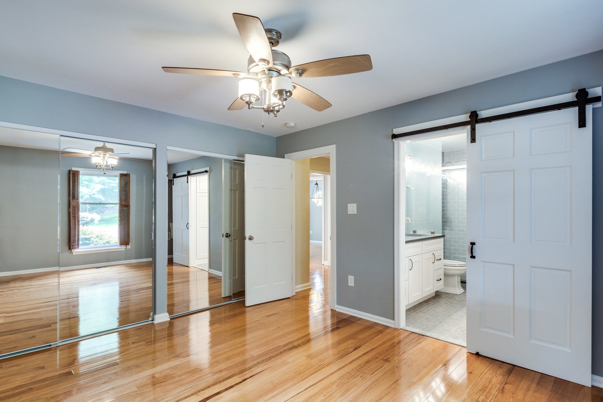 An empty bedroom with hardwood floors , a ceiling fan , and sliding barn doors.