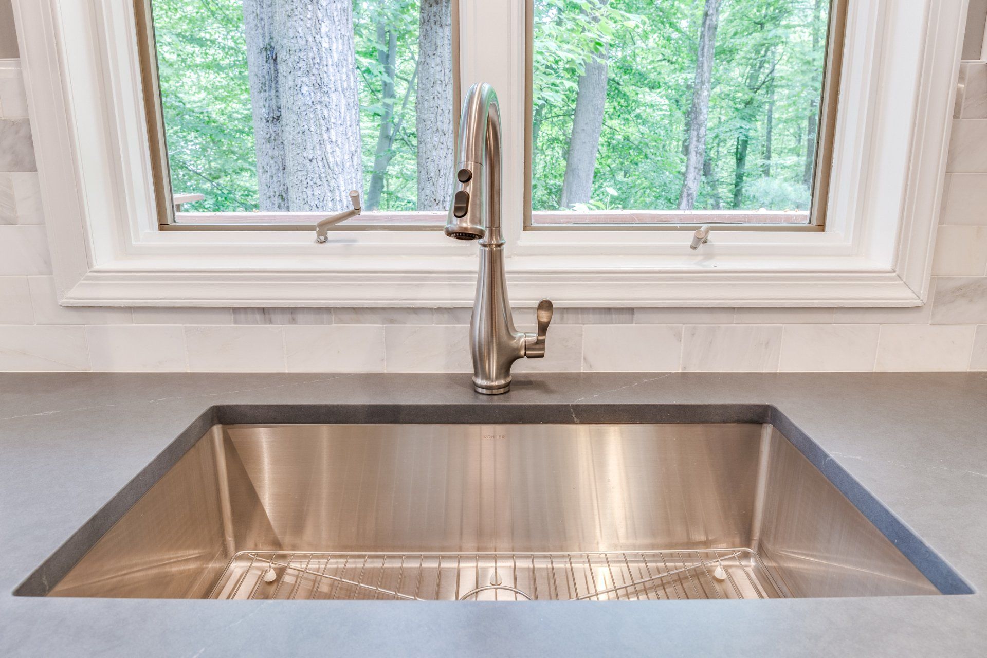 A stainless steel kitchen sink with a faucet and a window in the background.
