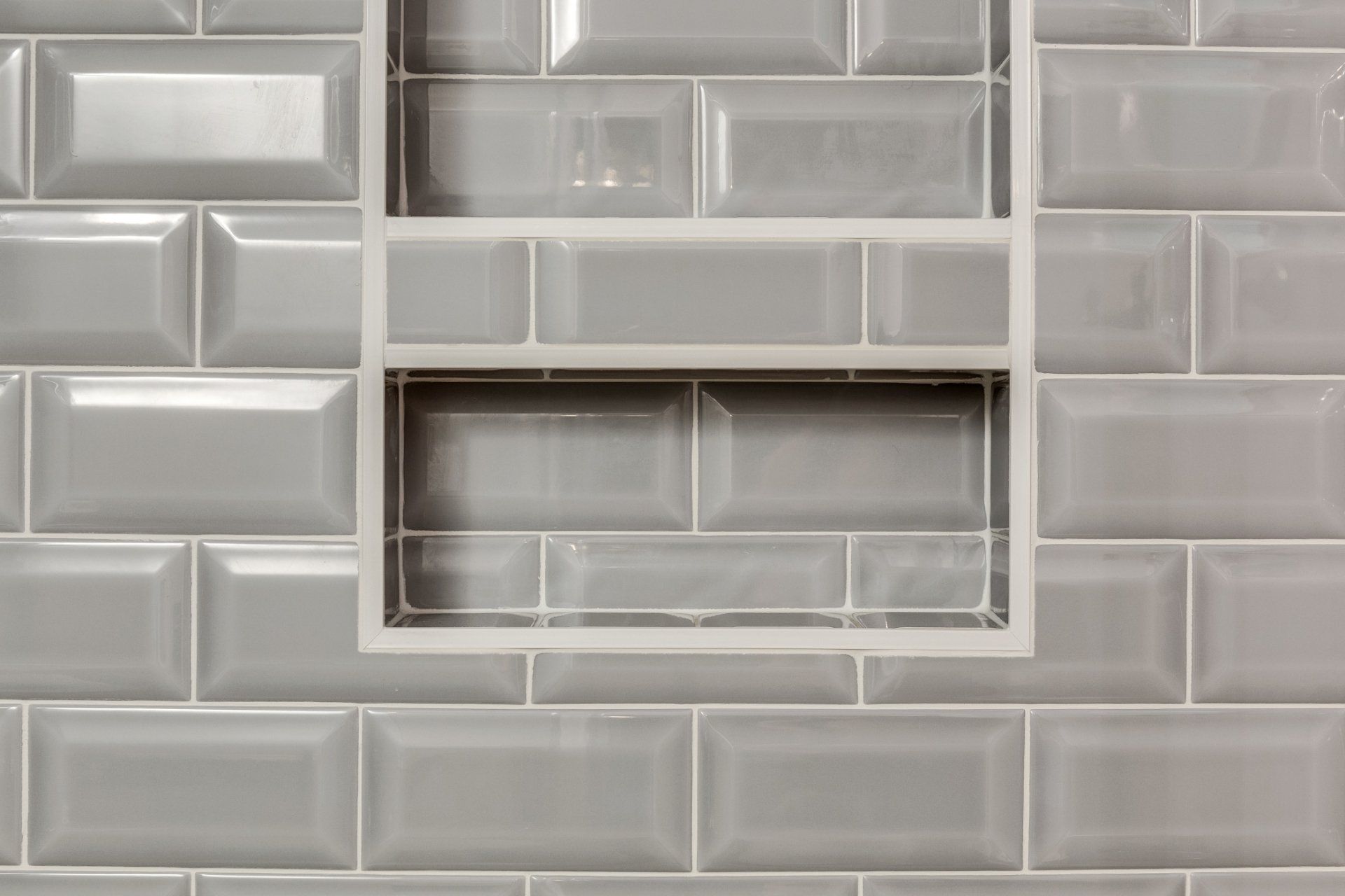 A close up of a bathroom wall with gray tiles and a shelf.