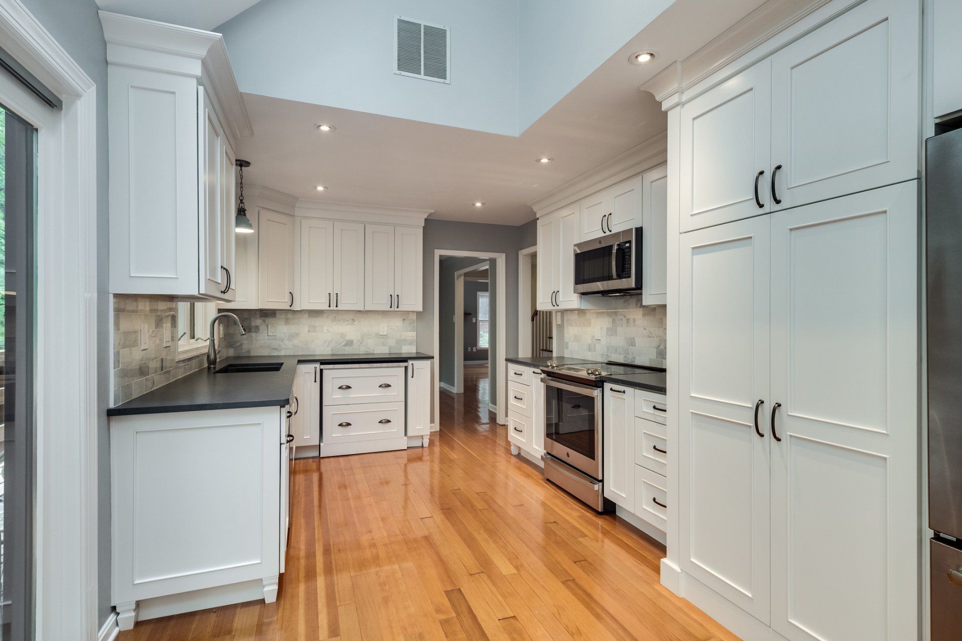 A kitchen with white cabinets and hardwood floors and stainless steel appliances.