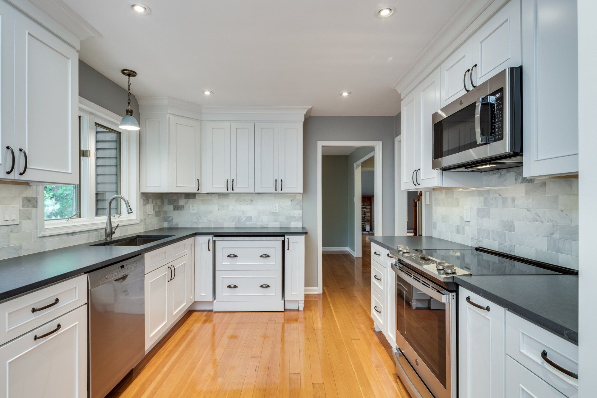 A kitchen with white cabinets , black counter tops , stainless steel appliances and hardwood floors.