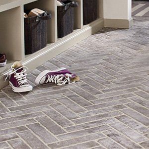 A pair of purple sneakers are sitting on a herringbone tile floor.