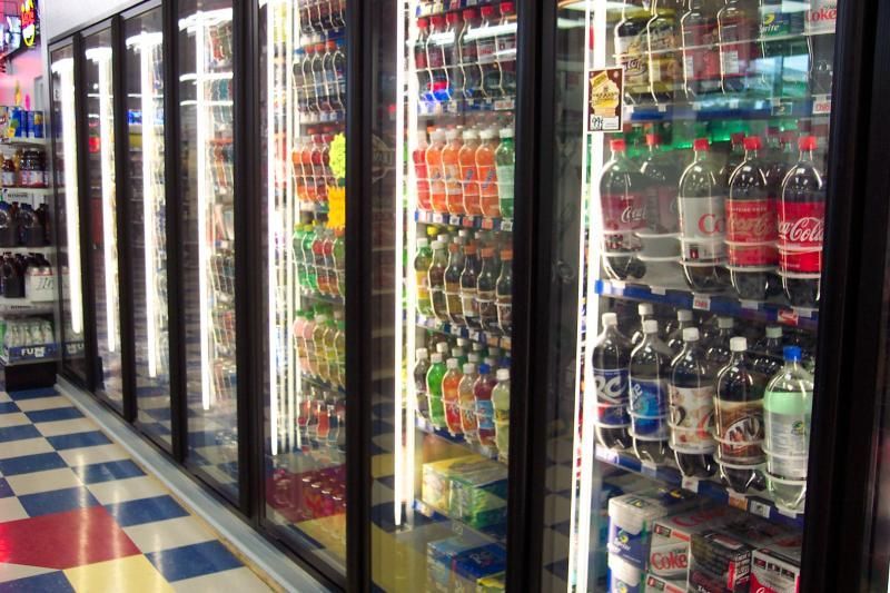 A row of refrigerators filled with bottles of soda including coca cola