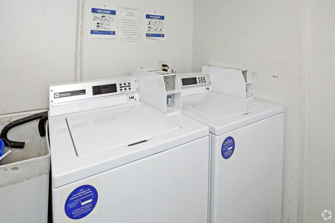 Two white washing machines are sitting next to each other in a laundry room.