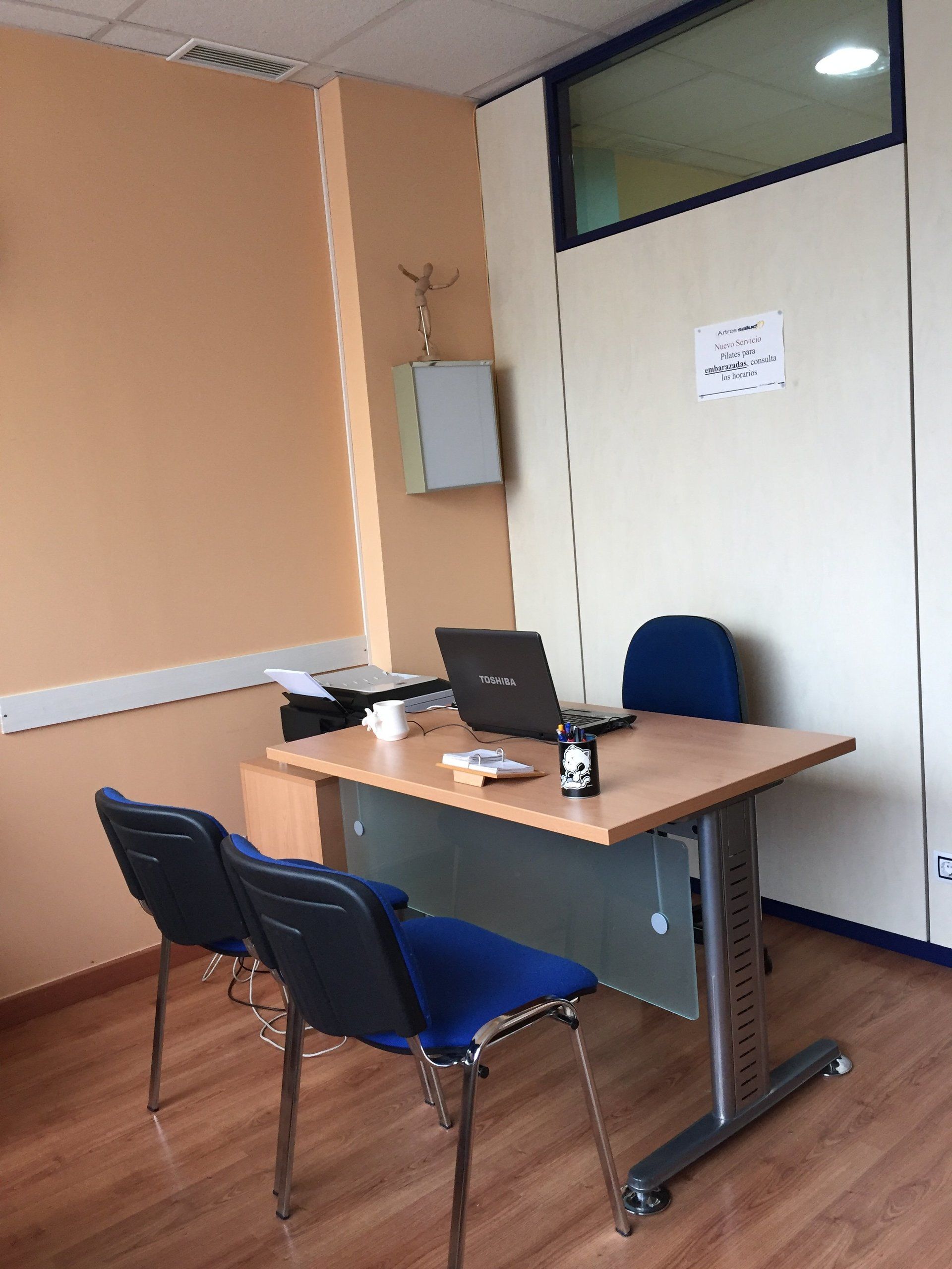 Una habitación con un escritorio, sillas y una computadora portátil encima.