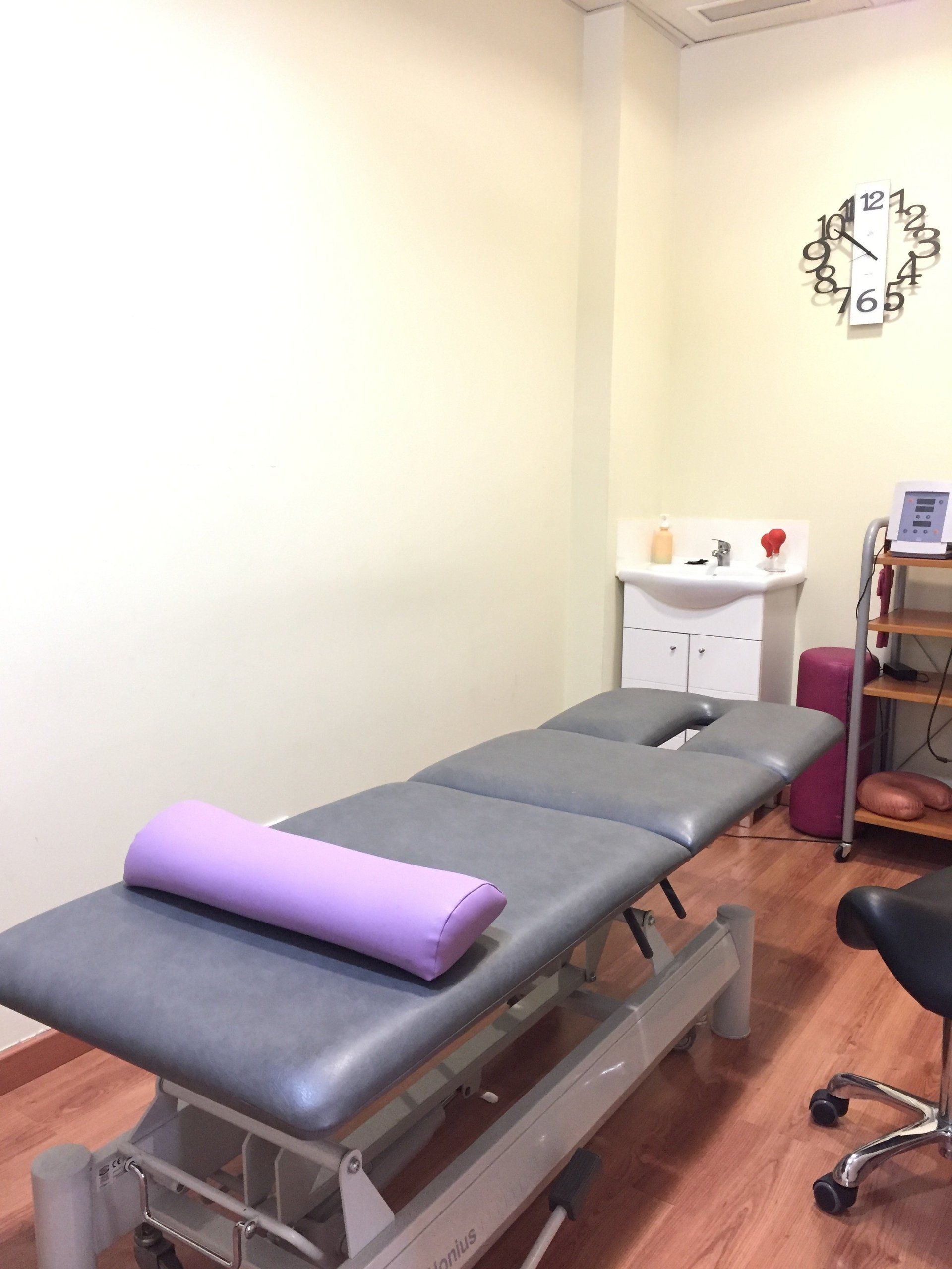 Una mesa de masajes con una almohada morada encima en una habitación con un reloj en la pared.