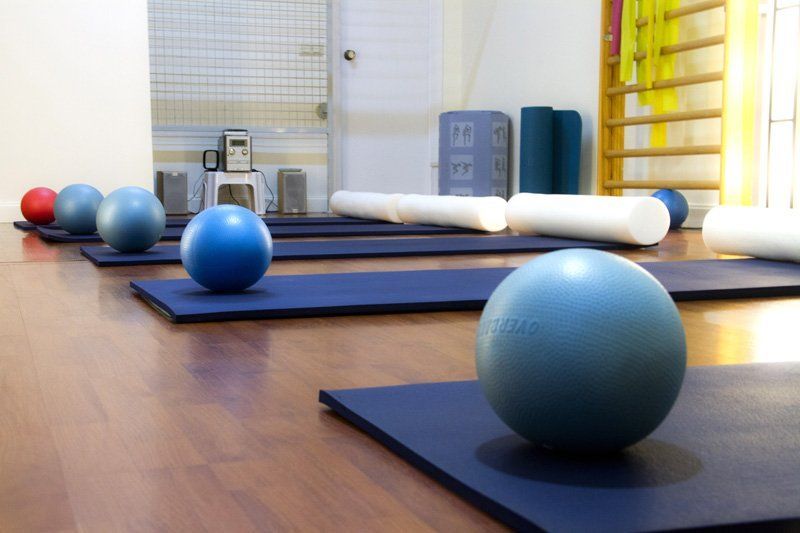 Una fila de colchonetas y pelotas de pilates en un gimnasio.