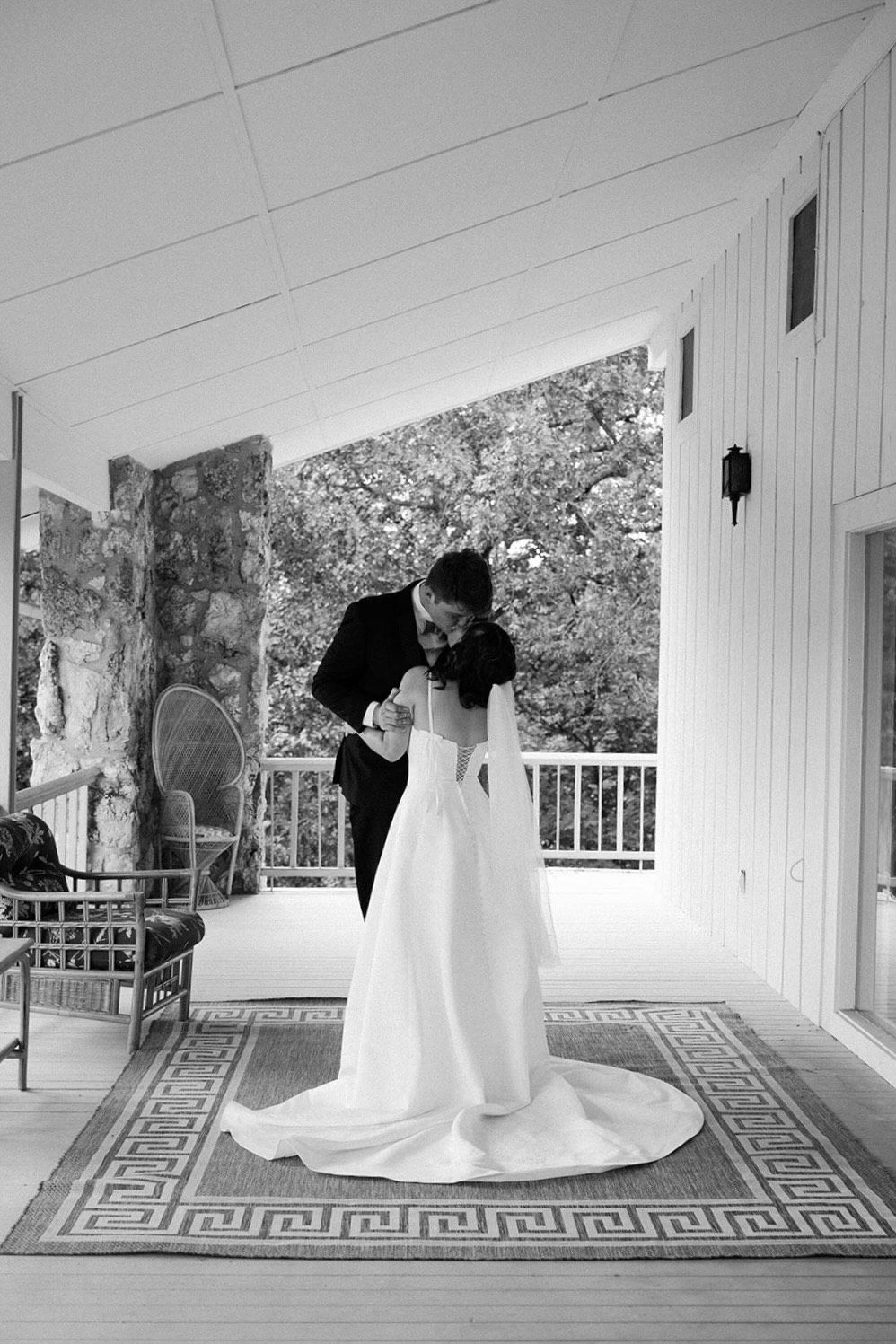 A bride and groom kissing while the bride holds a bouquet of white roses.