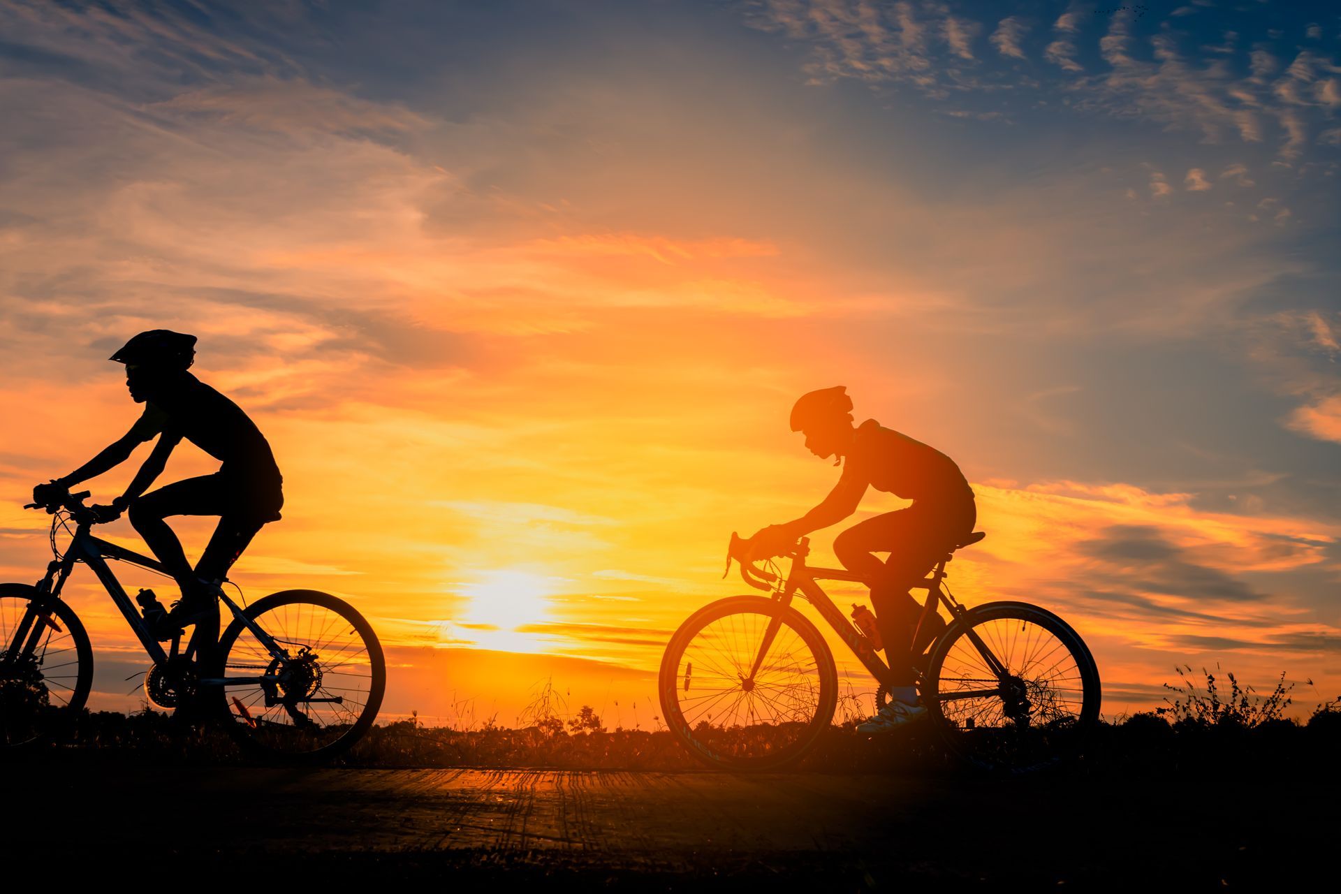 Two people are riding bicycles at sunset.