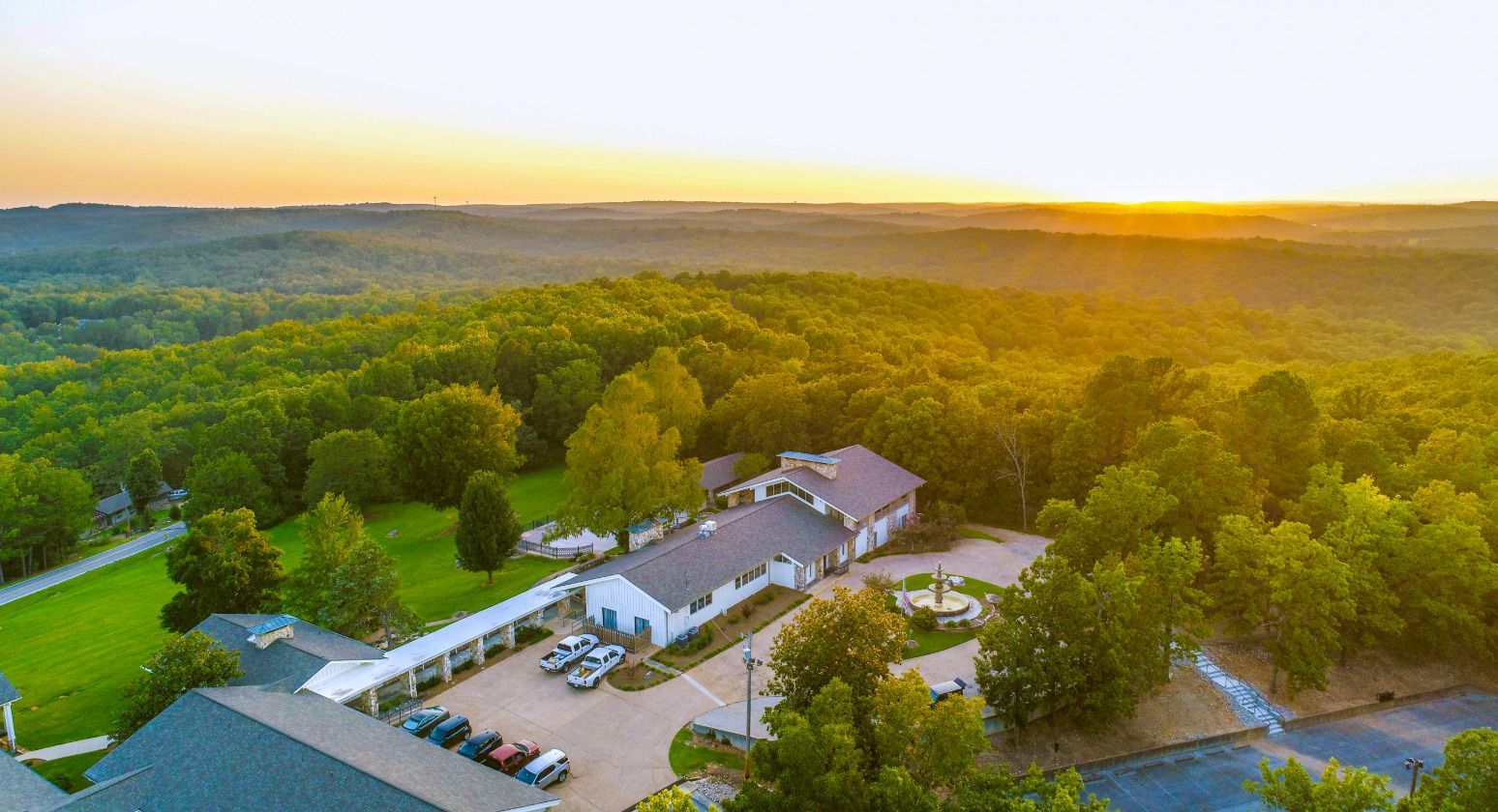 An aerial view of a house in the middle of a forest at sunset.