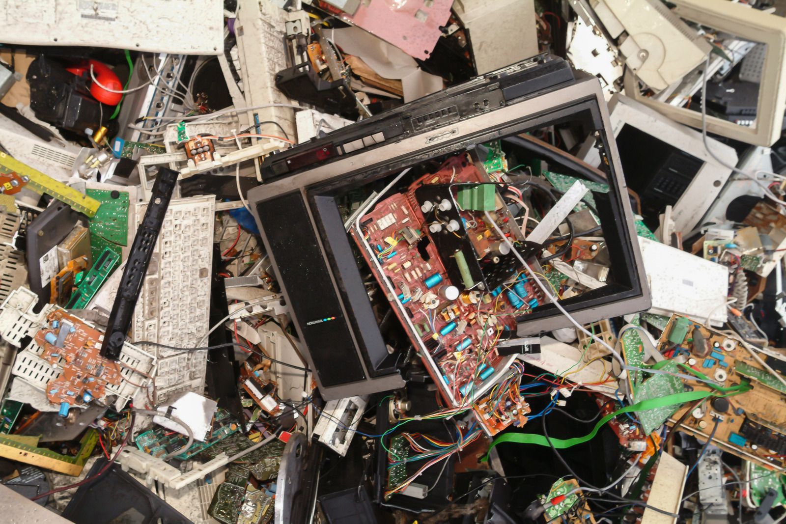A cluttered heap of discarded electronic waste, including circuit boards, broken computer monitors, and plastic components.