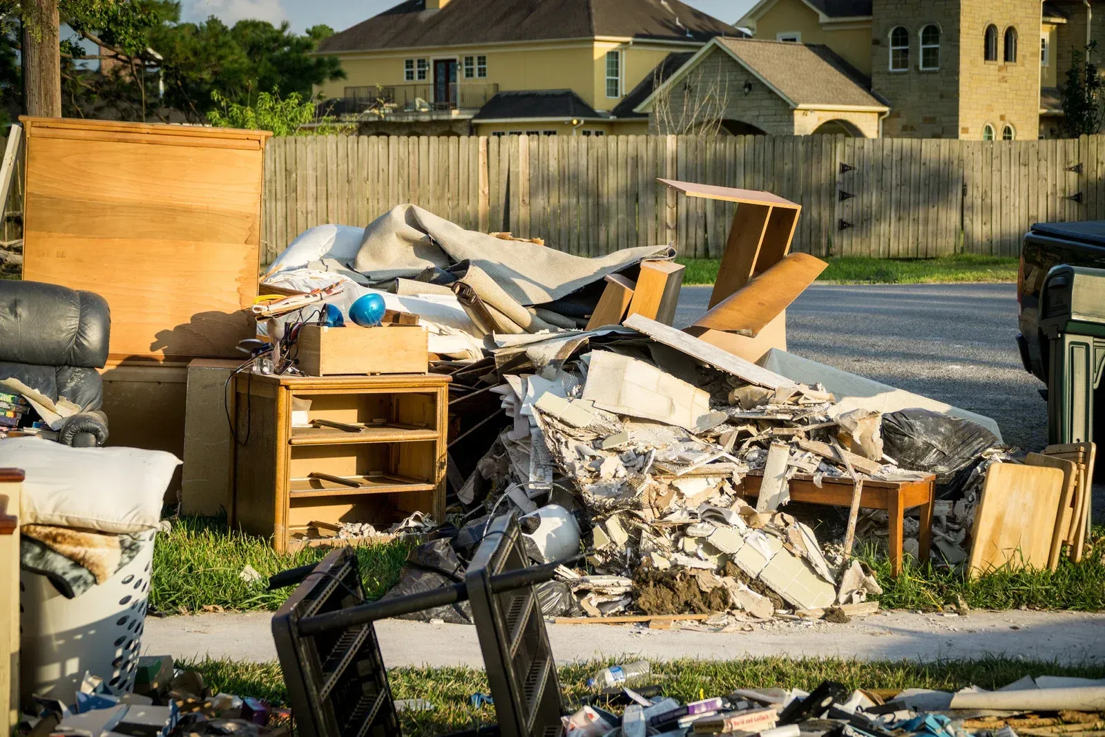 A large pile of household trash, debris, and discarded furniture sitting on a suburban curbside for collection.