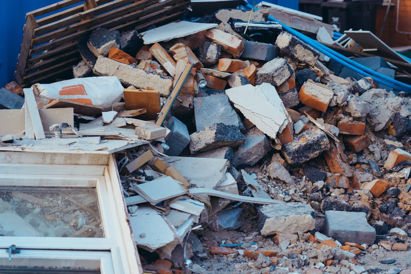 A pile of construction debris and rubble containing bricks, wood scraps, and a window frame sits outdoors.