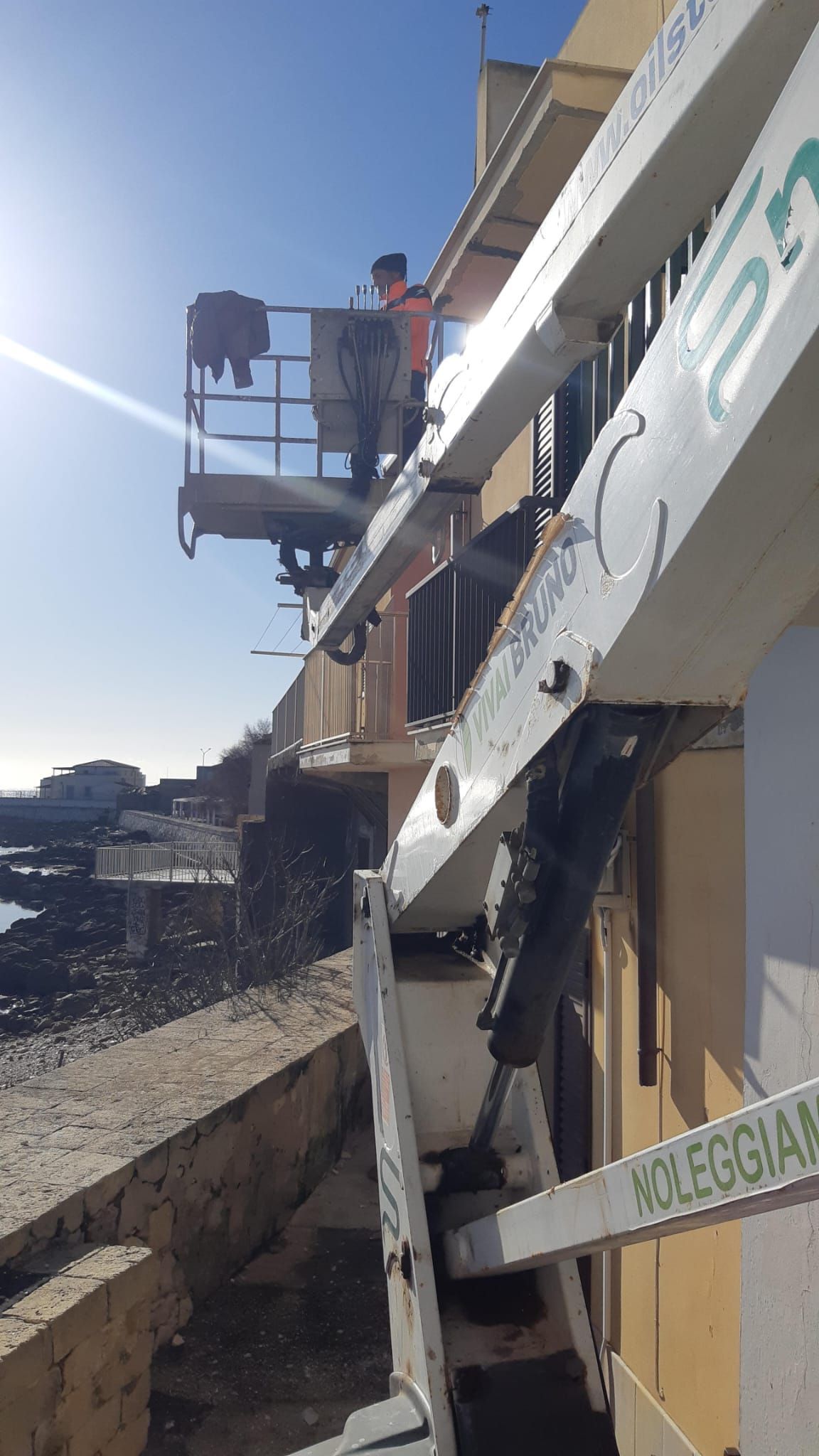 Uomo su un ascensore che lavora all'esterno di un edificio vicino al lungomare.