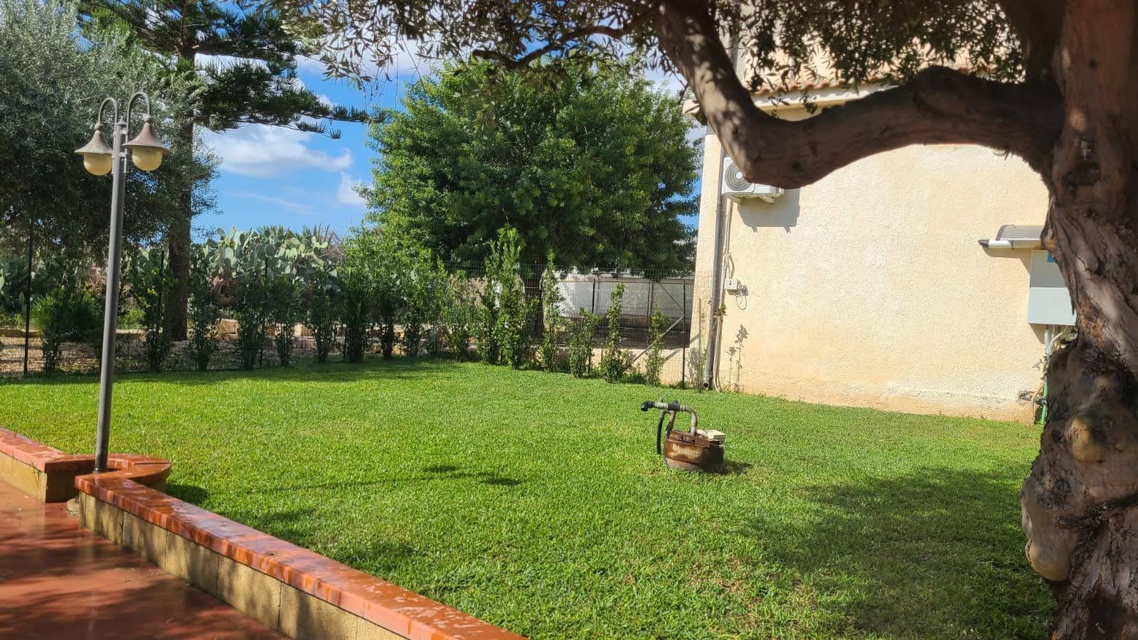 Un prato verde rigoglioso di fronte a un edificio chiaro con alberi e un piccolo tosaerba.