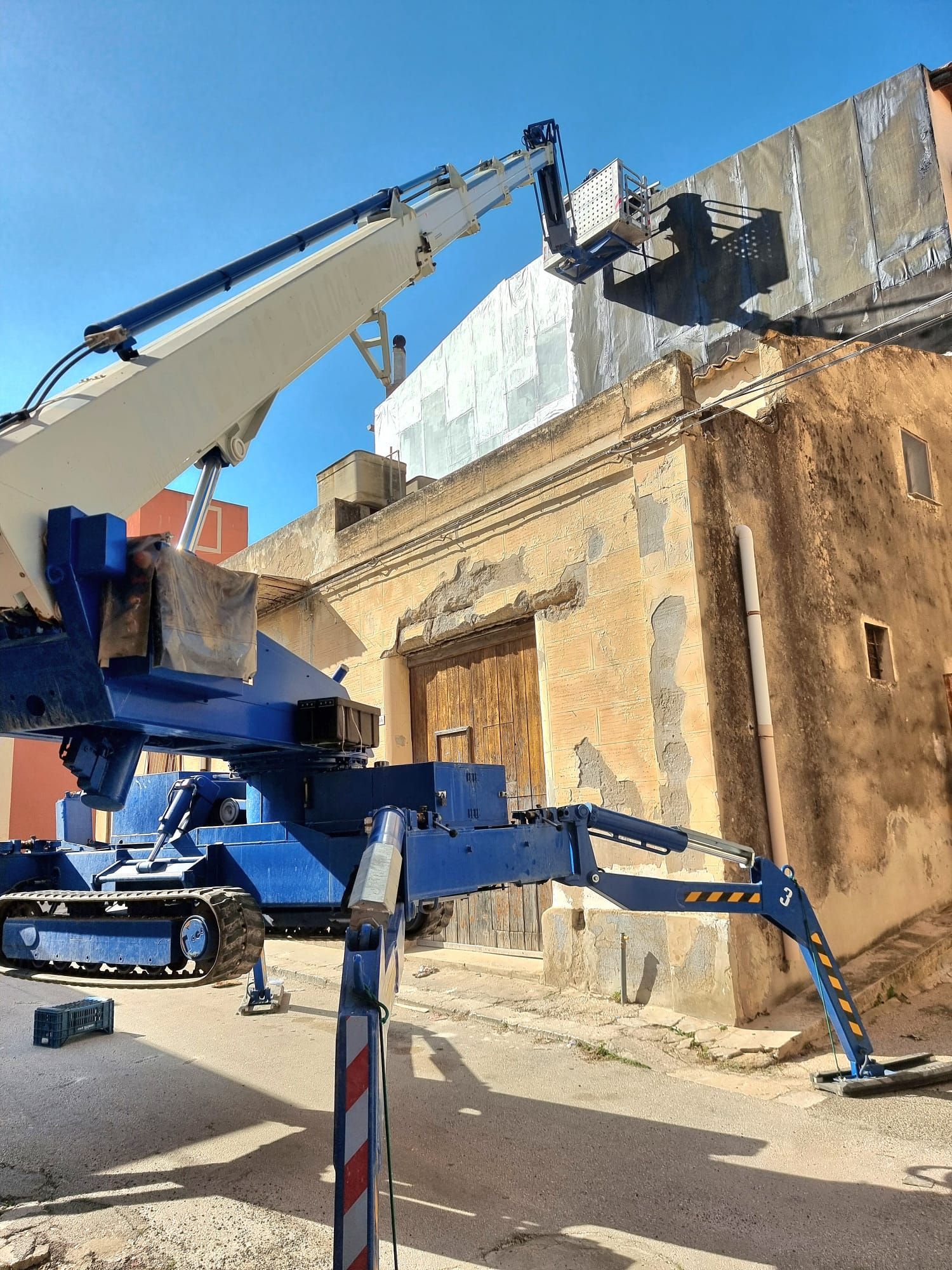 Ascensore blu da cantiere al lavoro su un edificio rovinato dalle intemperie; giornata di sole.