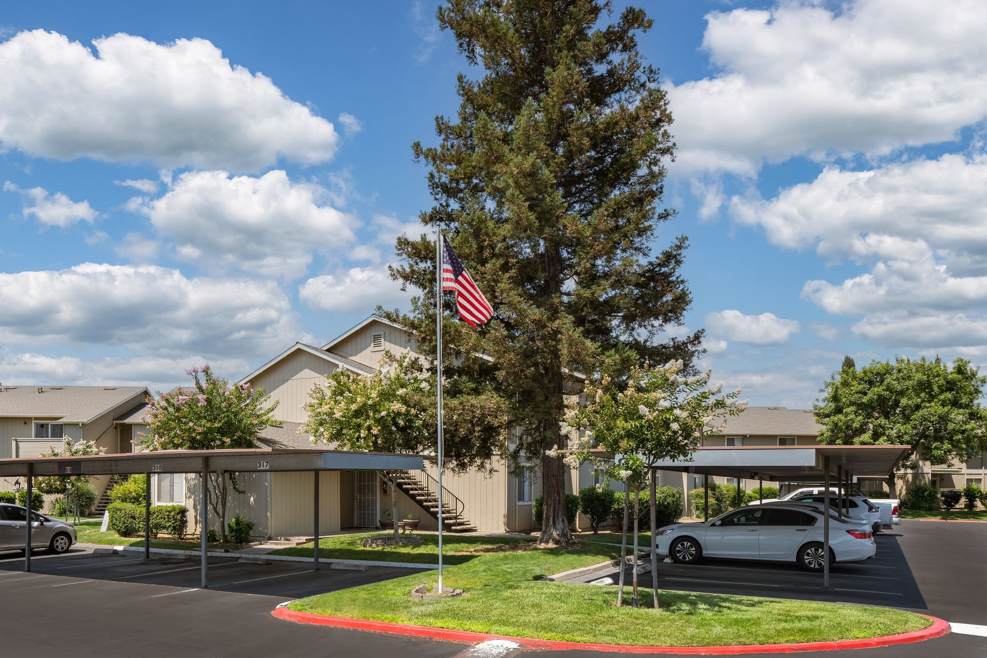 Apartment complex with a car port. Cars are parked under the canopy on a sunny day.