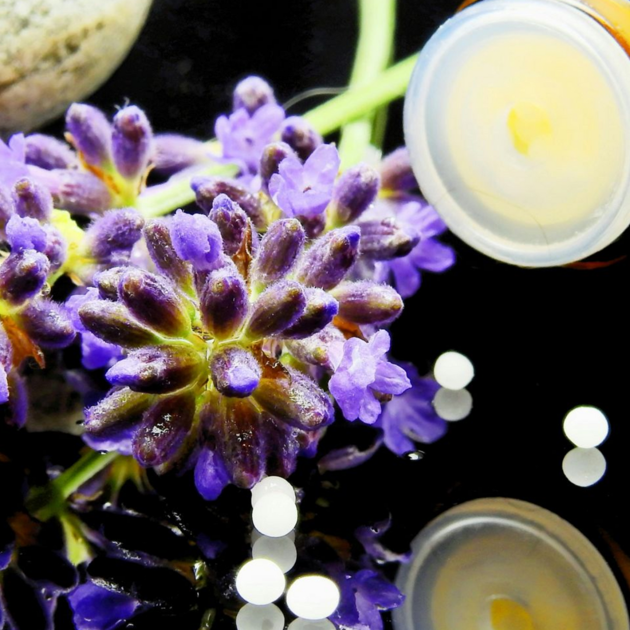Lavender flowers with two small cosmetic jars and white pearls on a black reflective surface.