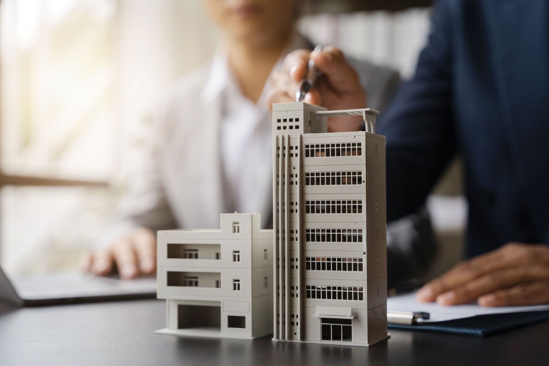 Two people examining a building model on a desk. One points at it with a pen.
