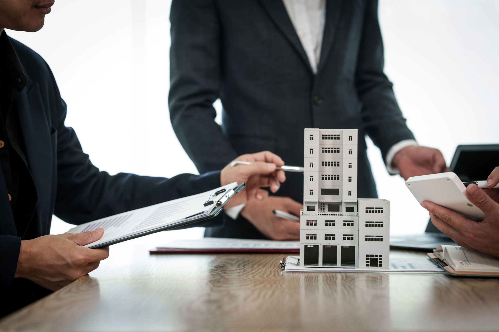 Businesspeople discussing building model at a desk. Hands pointing, using calculator and notepad.