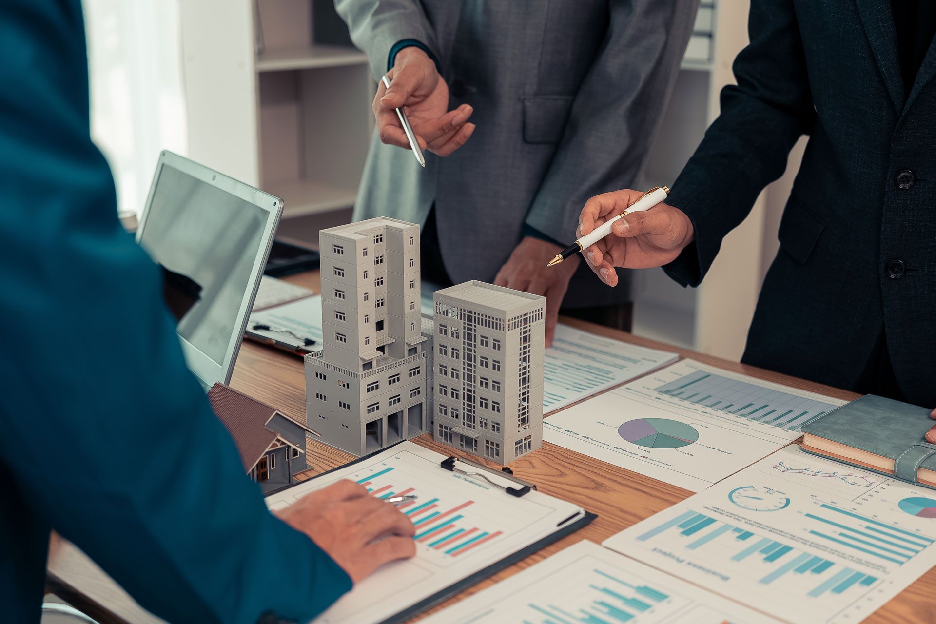 Three people in suits reviewing documents around a table with building models.