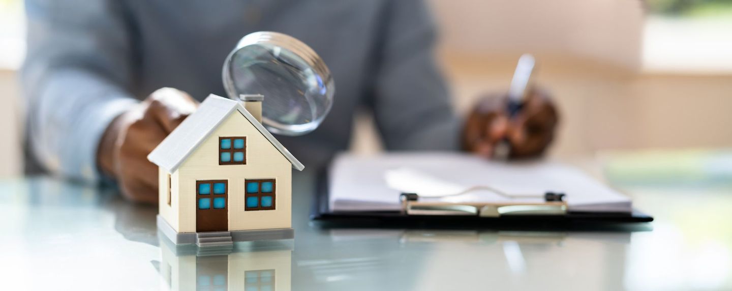 A person is sitting at a table with a magnifying glass and a model house.