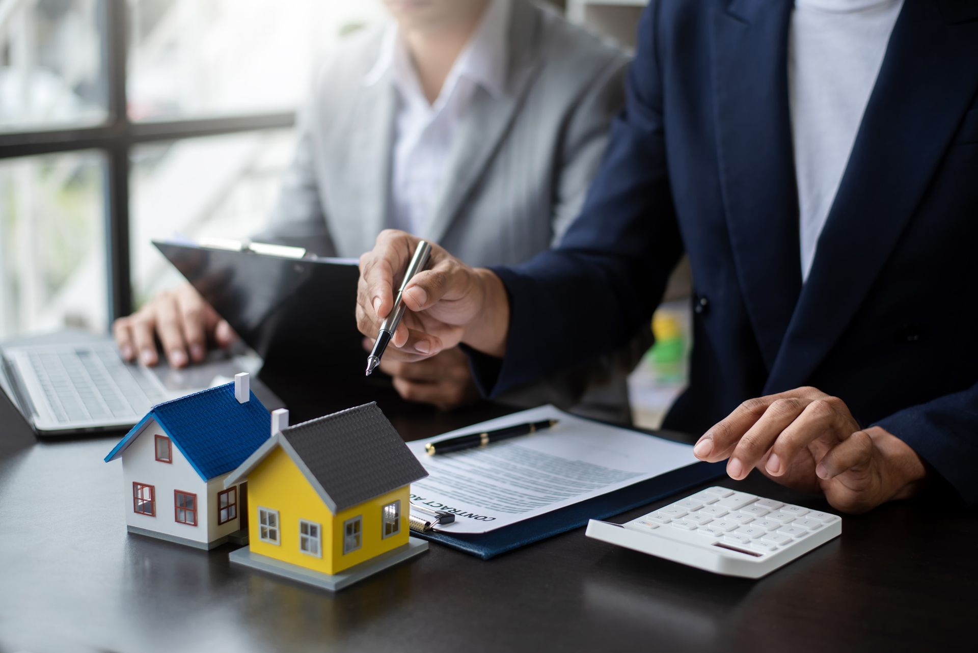 A couple of people are sitting at a table with a model house and a calculator.