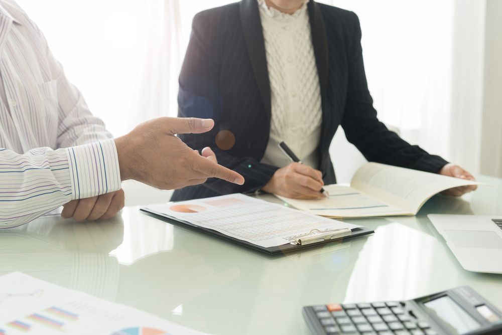 A man and a woman are sitting at a table with papers and a calculator.